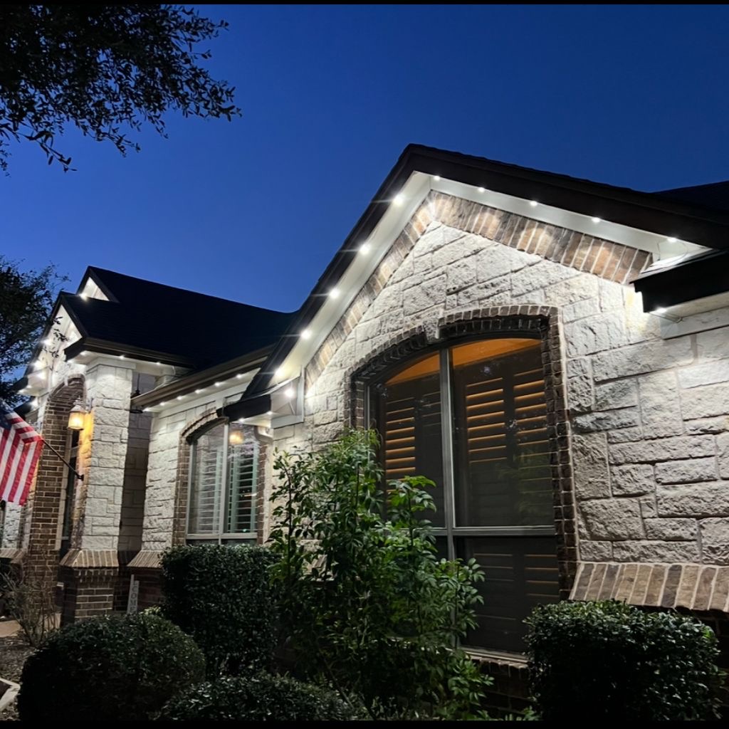 Stone home with white permanent roofline lights at dusk